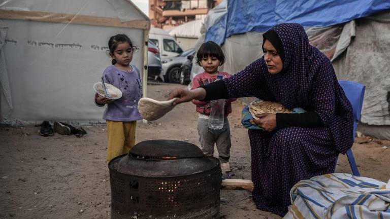 Una madre prepara comida para sus hijos en el exterior de su casa improvisada en un campo de refugiados de Khan Younis, Gaza.
