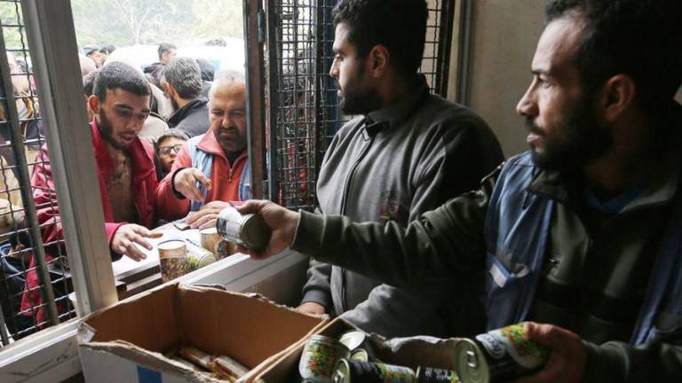 Los palestinos esperan en largas colas en una escuela de la UNRWA convertida en refugio mientras se distribuyen alimentos.