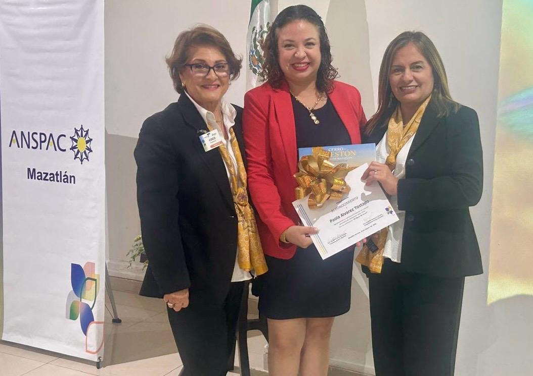 $!Coco Urrea de Valadés y Liz Benítez, presidenta y vicepresidenta de ANSPAC Mazatlán, respectivamente, hacen entrega de un reconocimiento a la expositora Paola Álvarez Tostado.