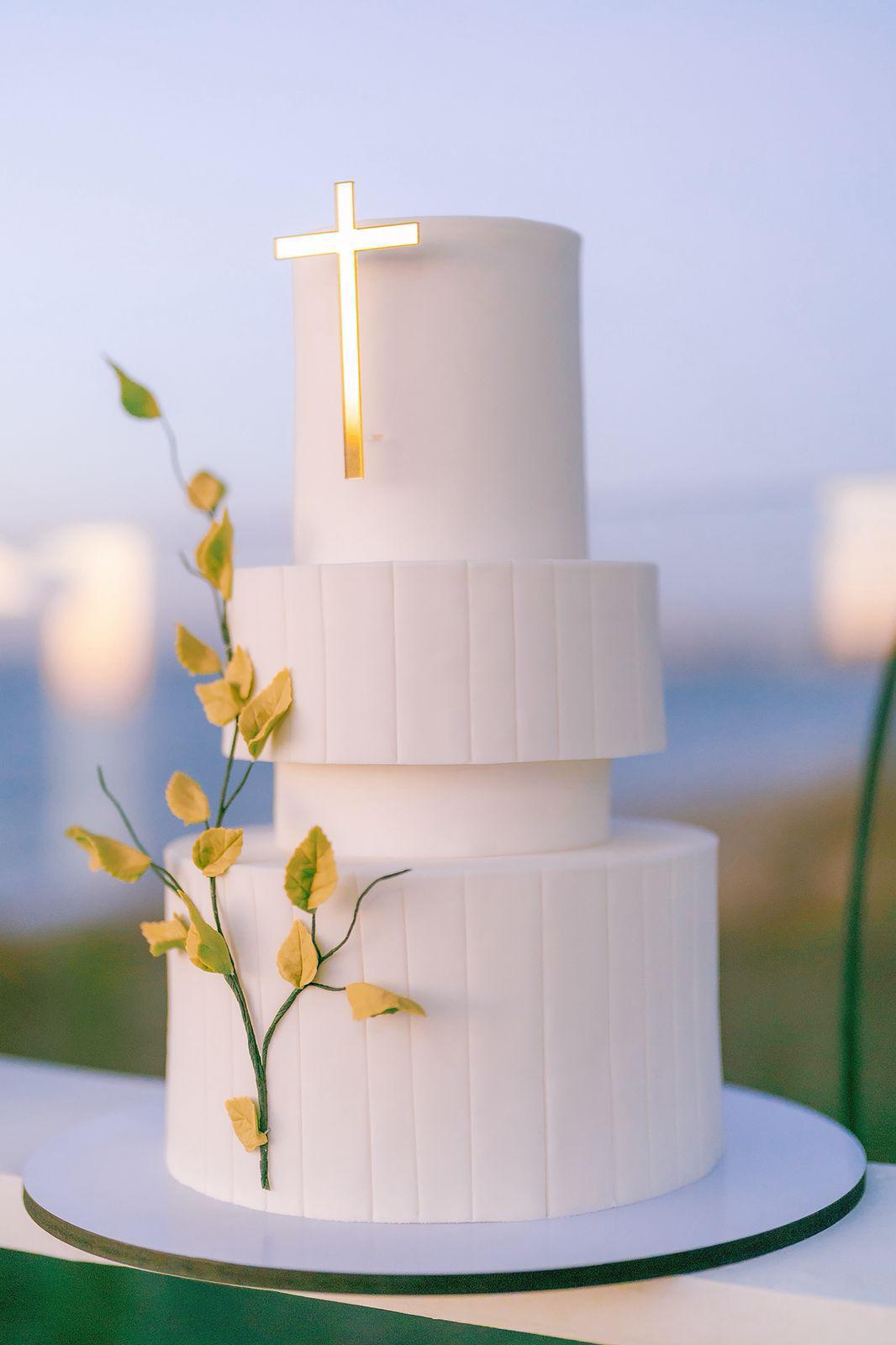 $!Un elegante pastel de tres niveles, adornado con una cruz y delicados detalles de hojas, formó parte de la fiesta.