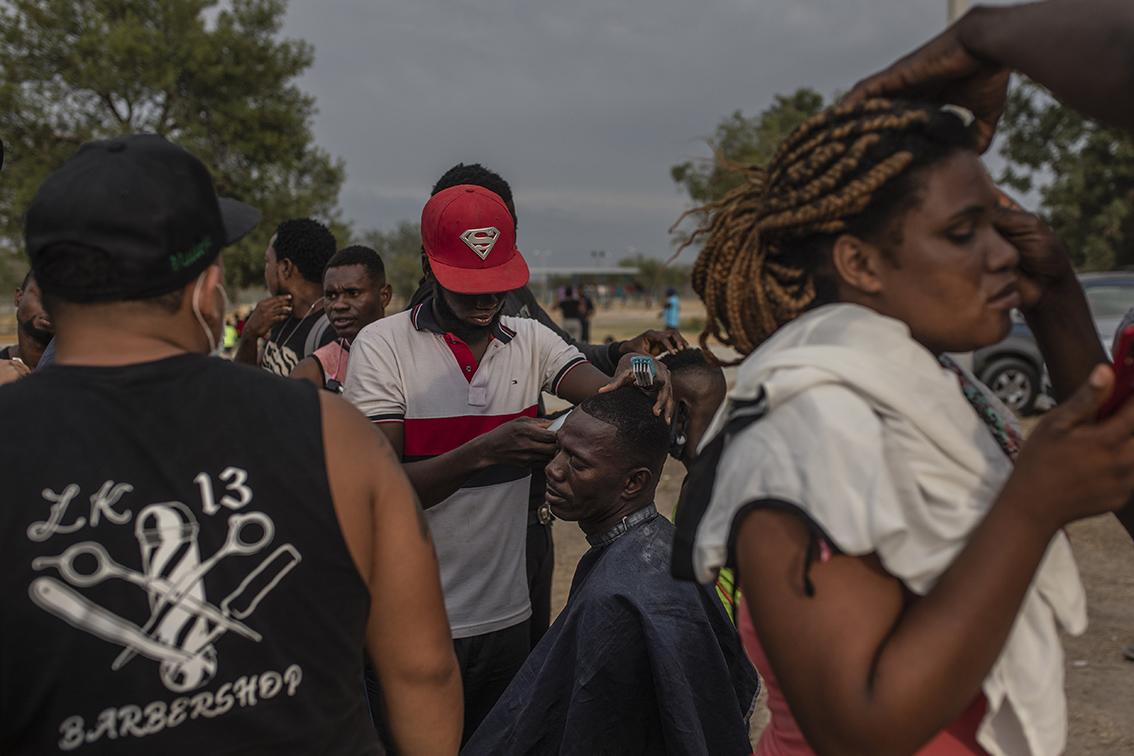 $!Migrantes, la mayoría de Haití, se cortan el pelo en un campo de refugiados improvisado en Ciudad Acuña, México.