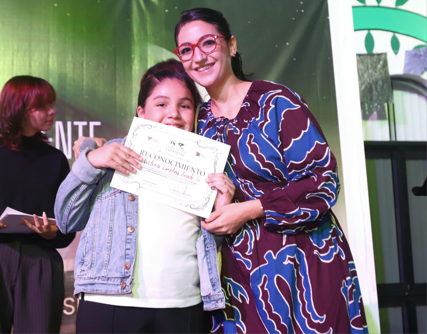 $!Victoria Tirado recibe su reconocimiento de manos de su maestra Kleyna Sarabia.