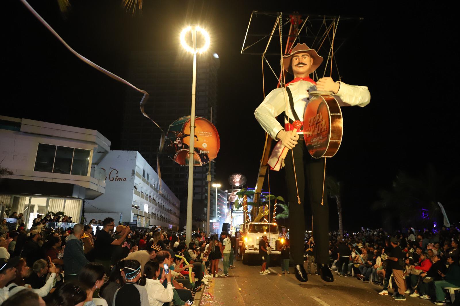 $!El Sinaloense”: Un gigante de nueve metros que, suspendido por hilos de acero, batió sus brazos al ritmo de la tambora, lanzando lluvias de confeti a su paso.