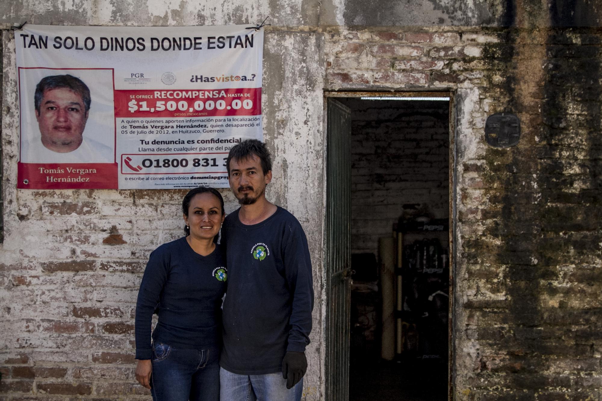 $!Mario y su hermana Mayra posan frente a la recicladora de la familia en Huitzuco, a fines de diciembre de 2018, junto a un cartel de la PGR que pide la cooperación ciudadana para localizar a su hermano Tomás, desaparecido el 5 de julio de 2012.