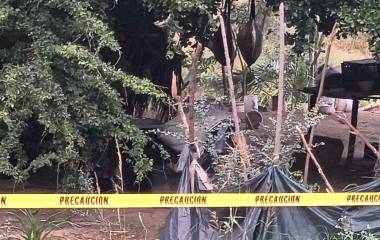 El hombre se encontraba inmóvil bajo la sombra de una vivienda construida con materiales rústicos al aire libre.