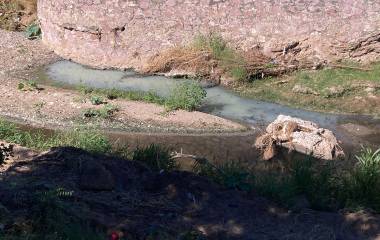 El líquido contaminado fluye desde una tubería y un boquete en el fondo del cauce, extendiéndose por el riachuelo y afectando la zona.