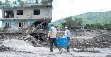 Trabajadores humanitarios transportan suministros pasando junto a una casa dañada por las inundaciones en Nepal.