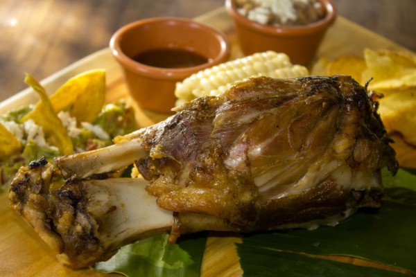 Chamorro con costra crocante por fuera, pero suave por dentro, con especias y notas de vino tinto, acompañada de elote cocido con mantequilla, guacamole, salsa, frijoles refritos y tortillas al comal.