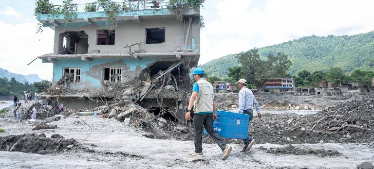 Trabajadores humanitarios transportan suministros pasando junto a una casa dañada por las inundaciones en Nepal.