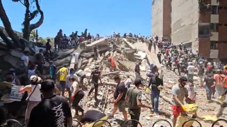 Voluntarios participan en la remoción de un edificio caído tras el sismo.