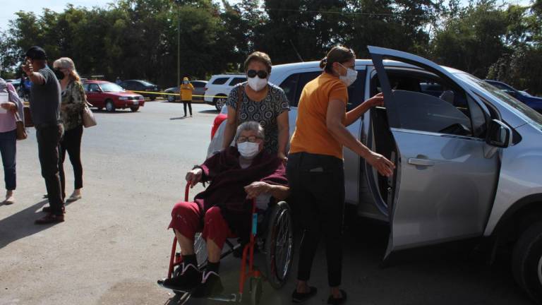 Una señora es trasladada en sillas de rueda a un centro de vacunación.