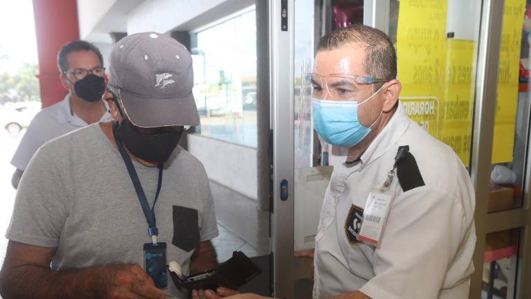 Un guardia de seguridad solicita el certificado de vacunación a las personas ingresar a una tienda de autoservicio.