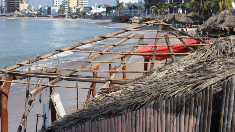 Comerciantes a la orilla de la playa en Mazatlán se apresuran a reconstruir las palapas dañadas por las marejadas recientes para volver a operar.