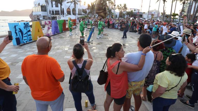 Mi Banda El Mexicano atrapa la atención de turistas y locales en la grabación del video musical Feliz, feliz en el malecón de Mazatlán.