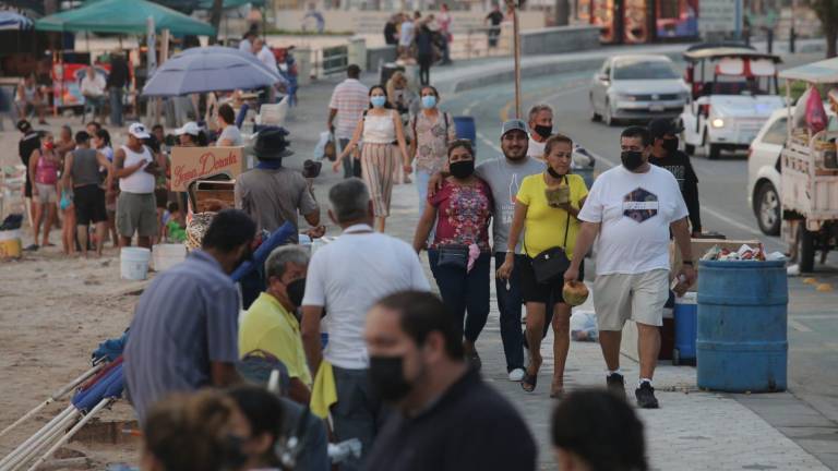 Gente camina por el malecón de Mazatlán, algunos sin cubrebocas.