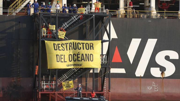Tripulación del Hidden Gem observa mientras activistas de Greenpeace suben a la escalera a bordo del barco donde desplegaron el mensaje “Destructor del Océano”.