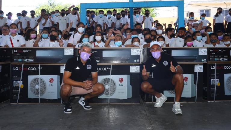 Bryan Colula y Marco Fabián posan con los minisplits donados en la Primaria de la colonia Urías.