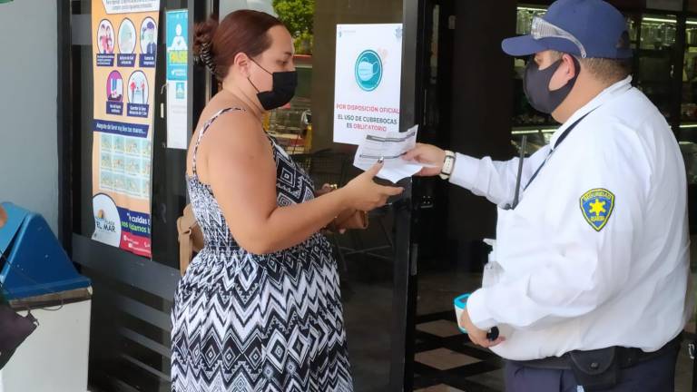 El guardia de seguridad de un restaurante solicita a una cliente el certificado de vacunación, y ésta se lo muestra.