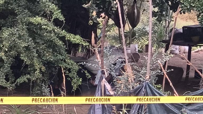 El hombre se encontraba inmóvil bajo la sombra de una vivienda construida con materiales rústicos al aire libre.