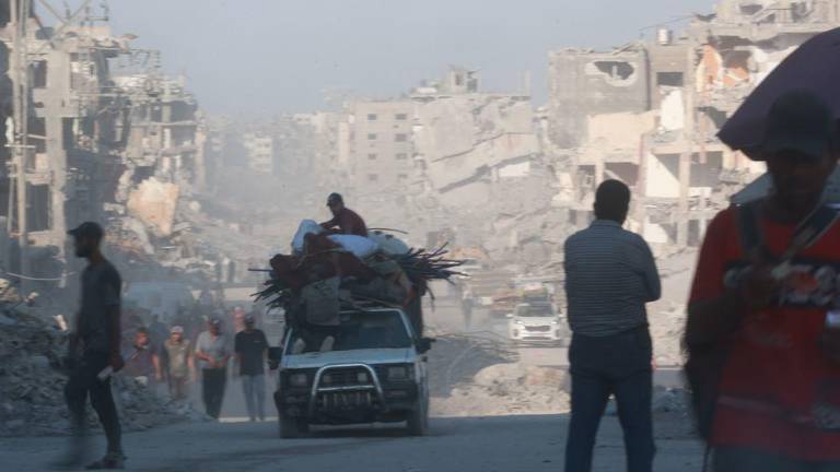 La gente se encuentra a la sombra de edificios destruidos en la Franja de Gaza.
