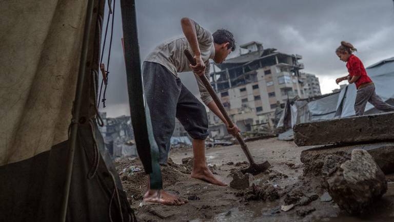 Un niño limpia la entrada de una tienda de campaña tras las fuertes lluvias en Gaza.