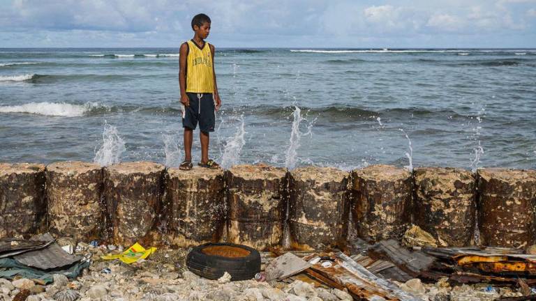 Un niño en el dique que protege el hogar familiar de las mareas crecientes del atolón de Majuro en las Islas Marshall.